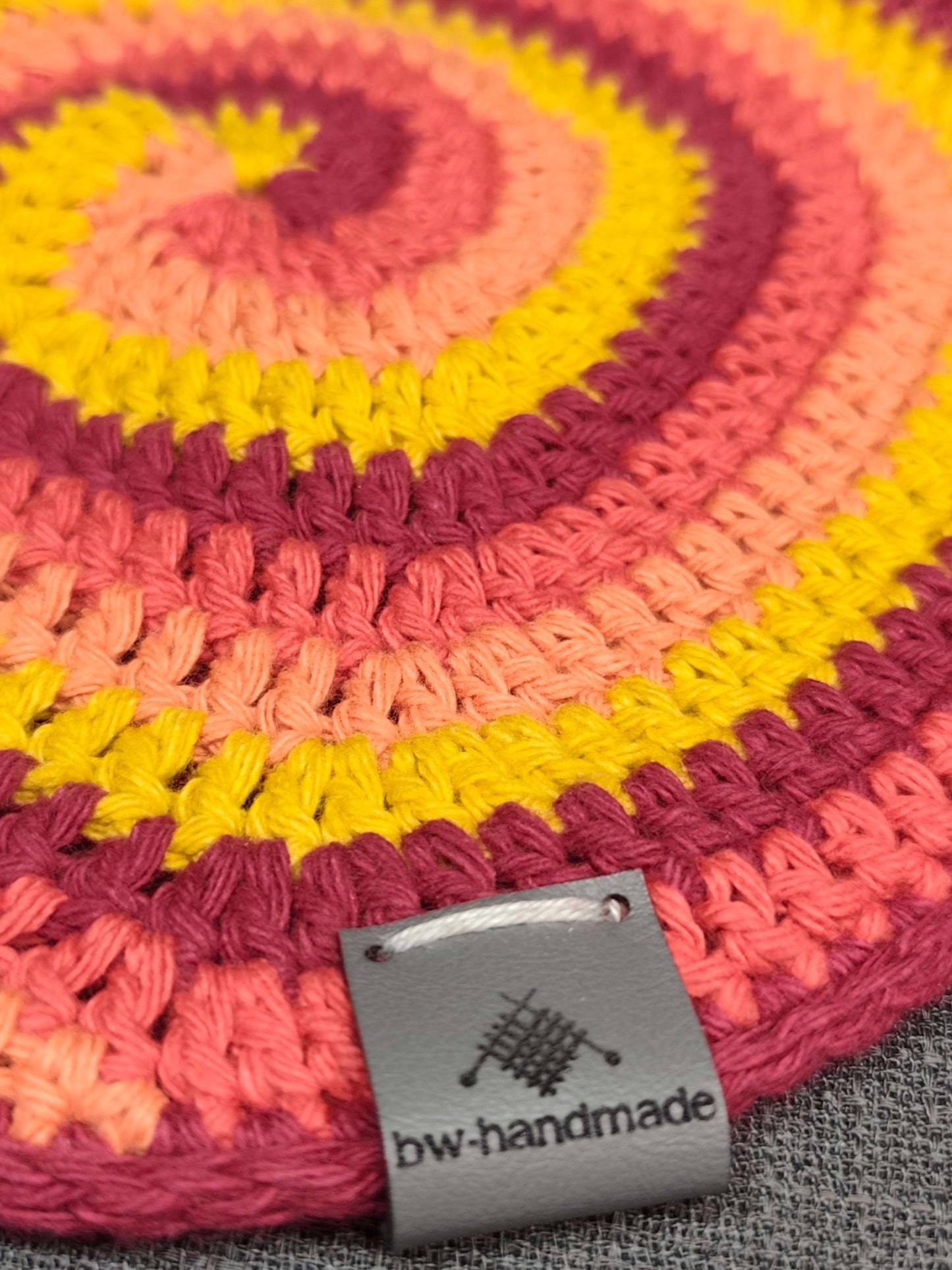 Detail des gehäkelten Spiralmusters in Gelb, Orange, Rot und Dunkelrot mit bw-handmade Label