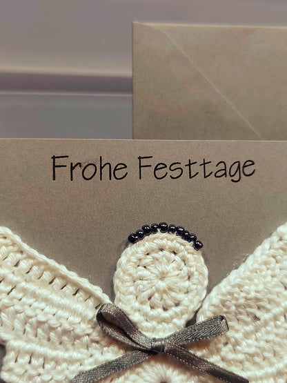 Detailaufnahme des gehäkelten Engels mit Perlen und Schleife auf Weihnachtskarte.